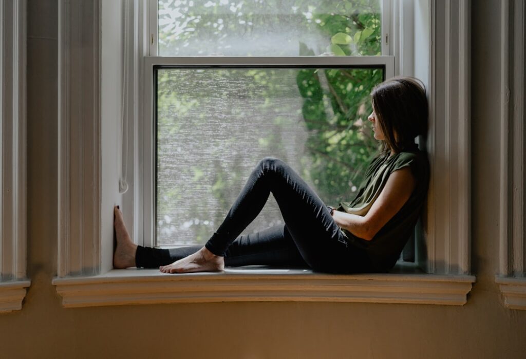 Person sitting by a window experiencing anxious thoughts